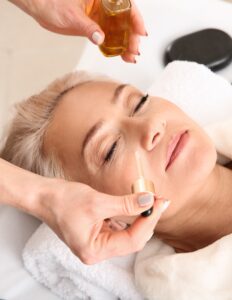 Mature woman undergoing treatment with face serum in beauty salon